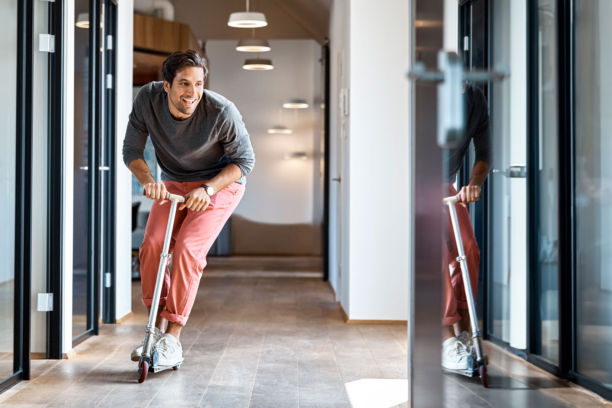 En glad man åker kick-bike i kontorskorridoren
