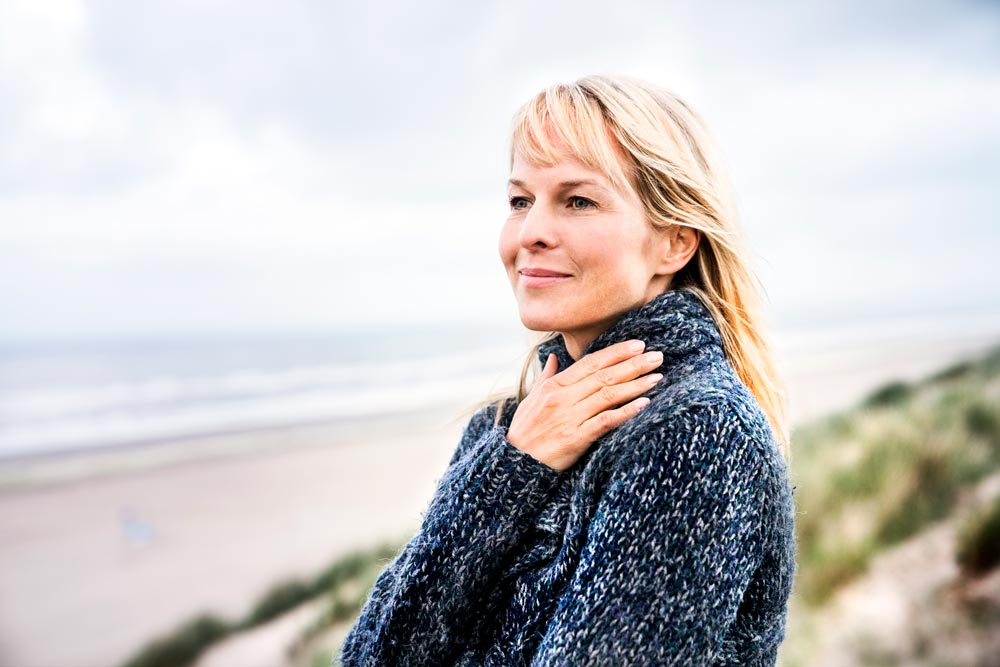 Kvinna som står på stranden och blickar ut mot havet.