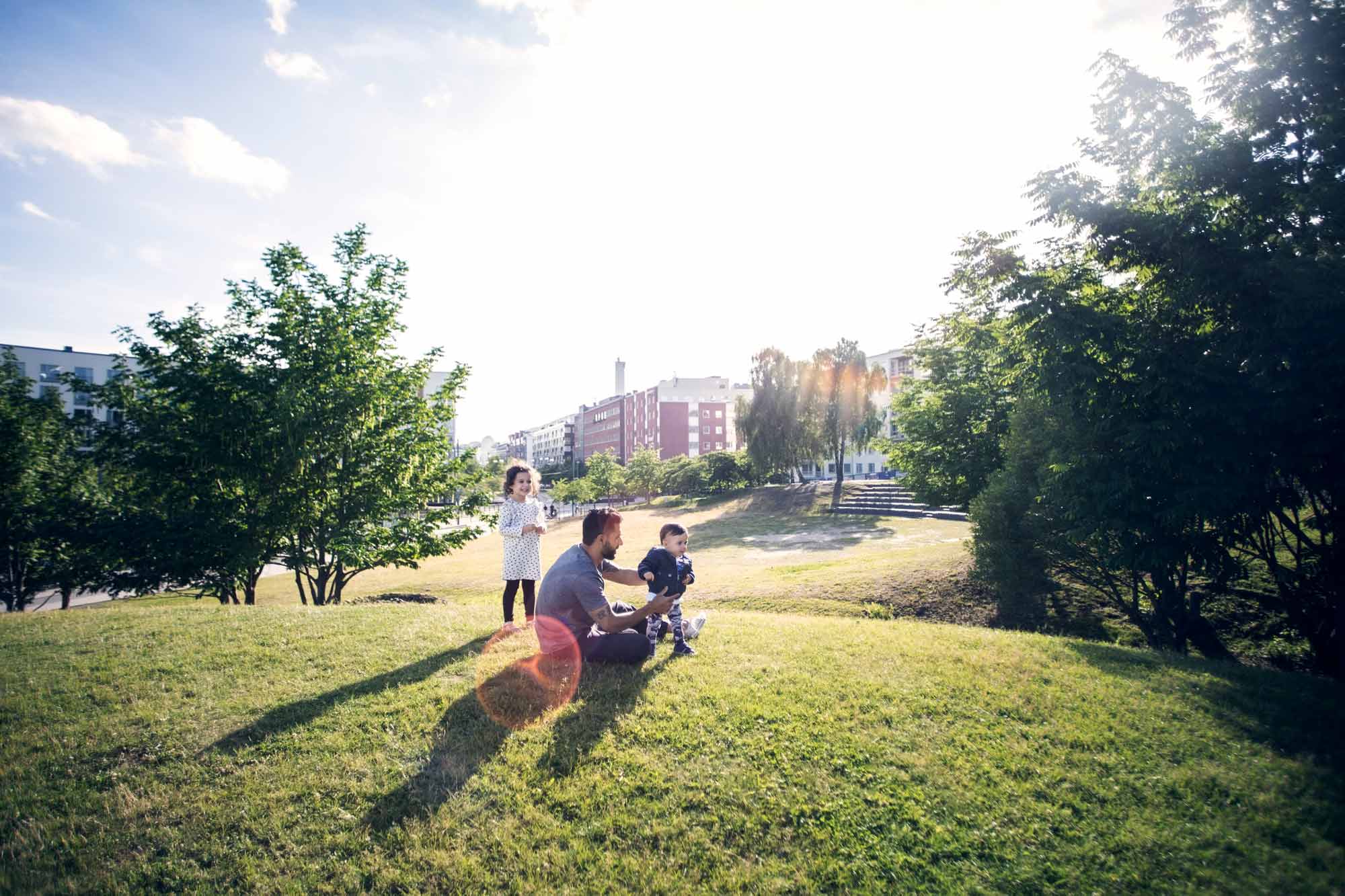 En familj sitter och njuter av vädret i en park i ett bostadsområde.