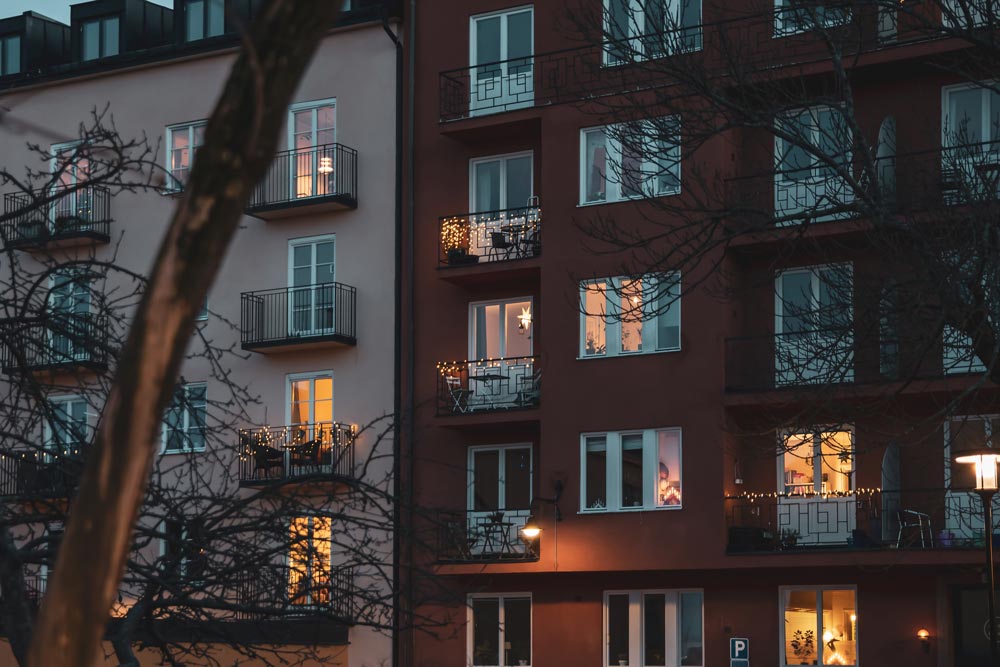 En stämningsfull vinterkväll i Stockholm visar en flervåningsbyggnad dekorerad med gula ljusgirlanger som lyser upp fönster och balkonger i flera våningar
